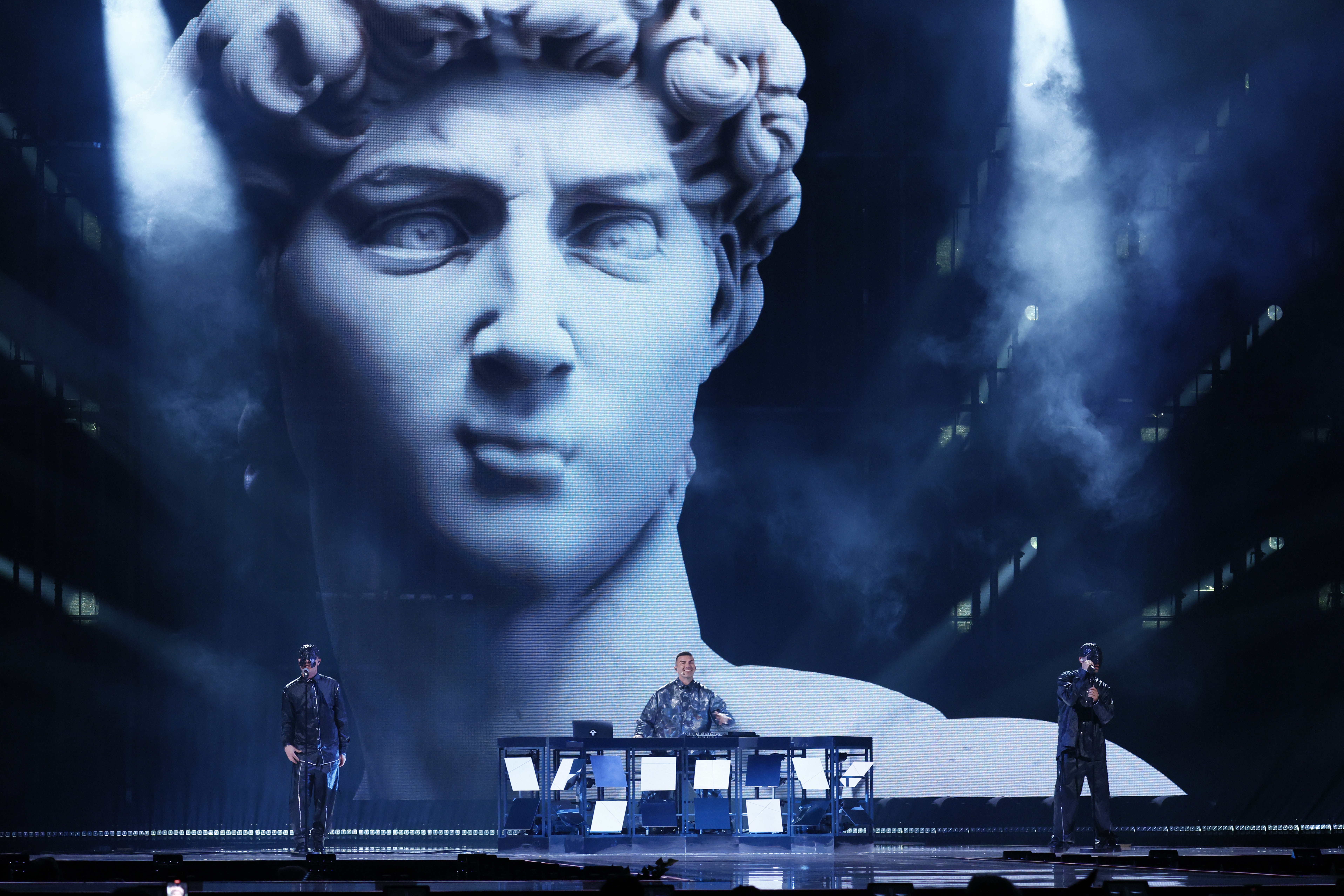 DJ and singer perform in front of a large video screen showing an animated statue of David.