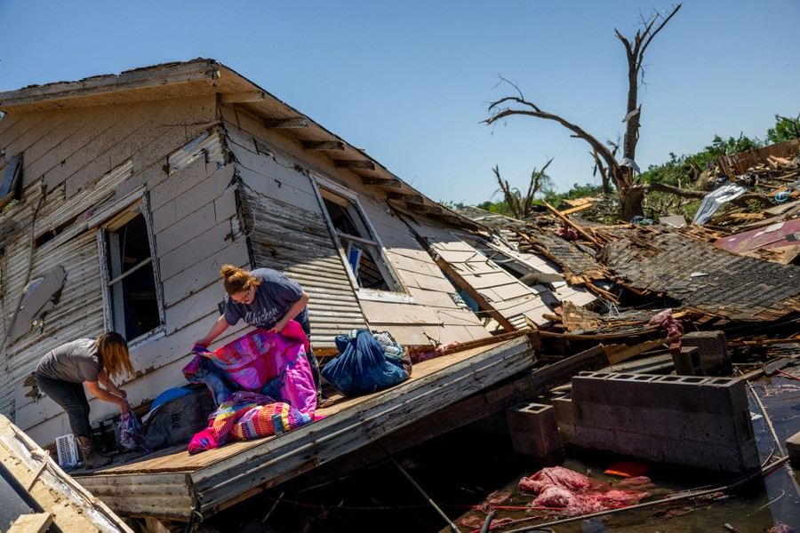 Two people sort through belongings amid storm-destroyed homes and debris.