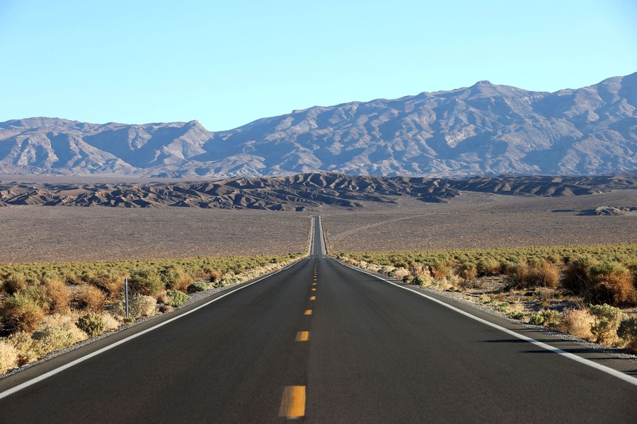A road runs toward the horizon in an arid landscape with mountains in the distance.