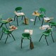 A mini circle of greenish chairs pinch attached desks and penning tools
