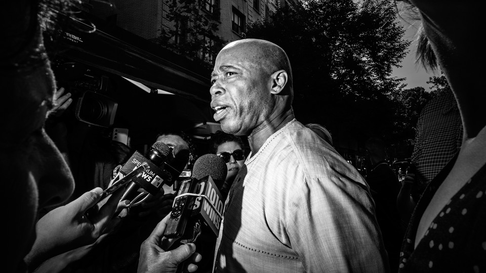 A black-and-white photo of Eric Adams being questioned by the press.