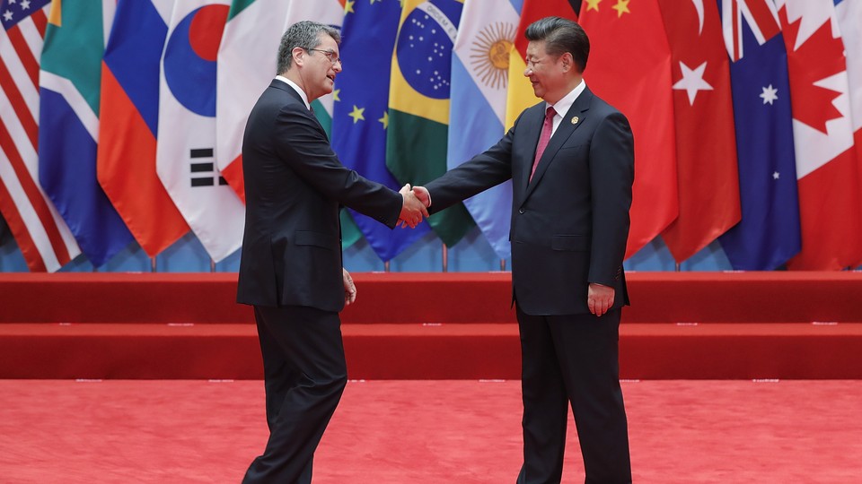 Director-General of the World Trade Organization Roberto Azevêdo shakes hands with Chinese President Xi Jinping on a red stage in front of several countries' flags at the G20 Summit in 2015.