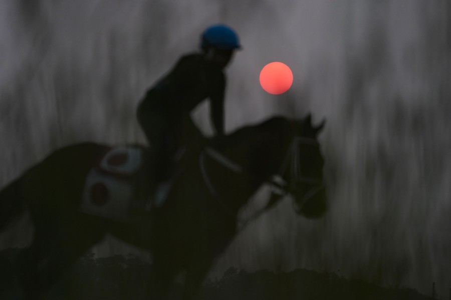 A reddish sun is seen beyond a rider on a horse.