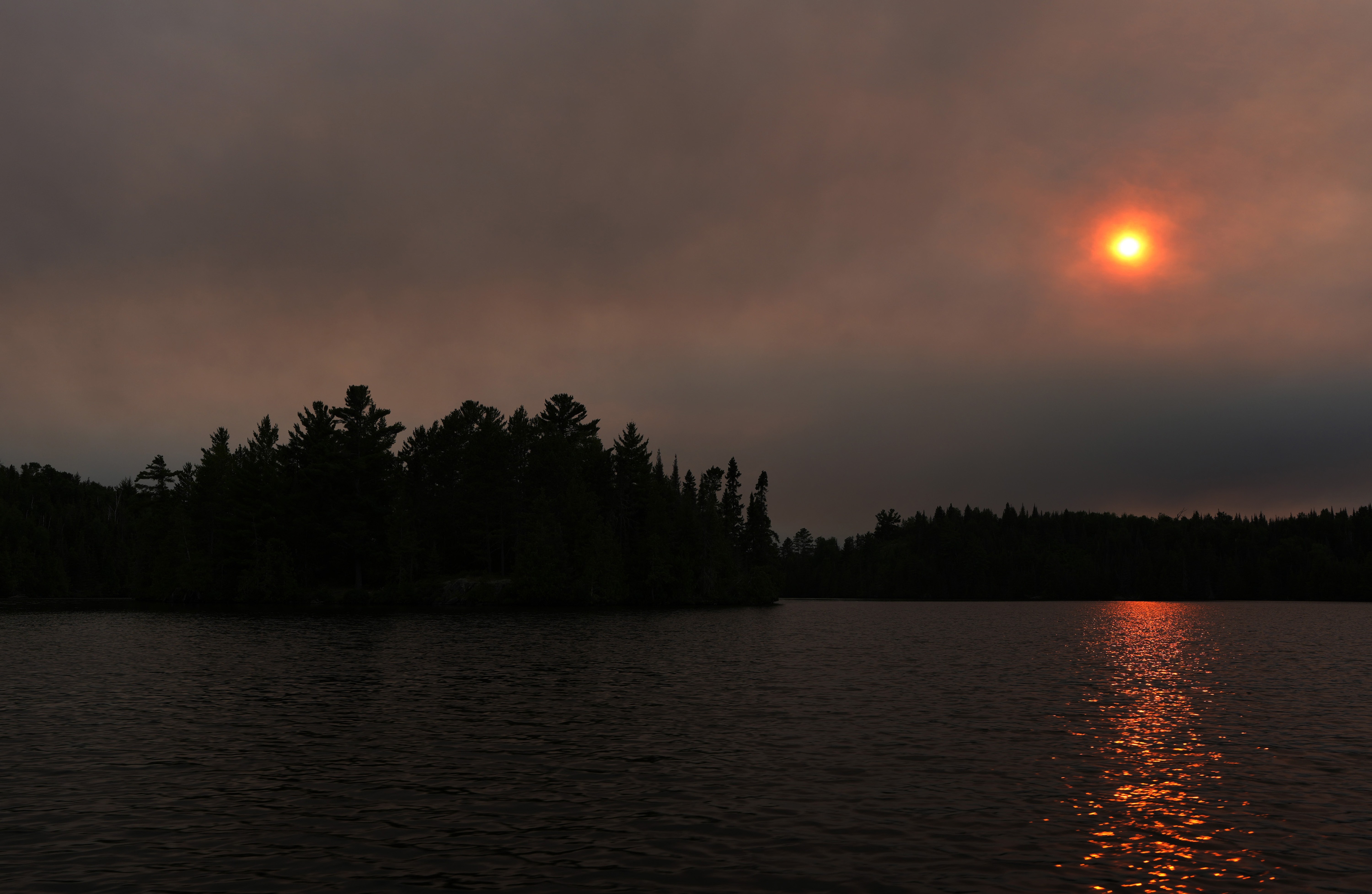 A dark-orange-colored sun, setting in a smoky sky