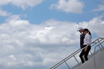 Donald Trump and Melania Trump walk down stairs leading off of an airplane.