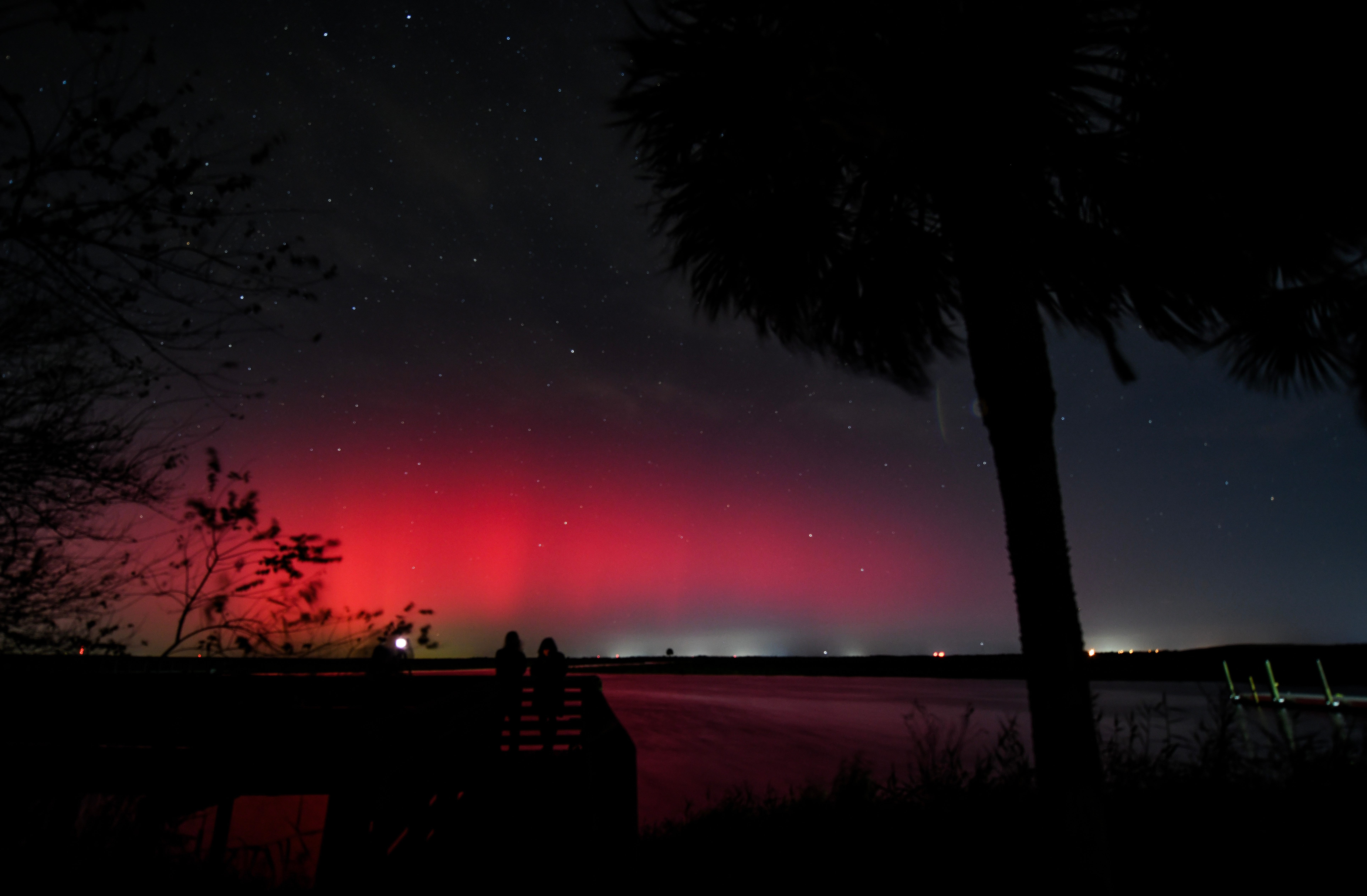 Several people look toward a glowing aurora in the distance.