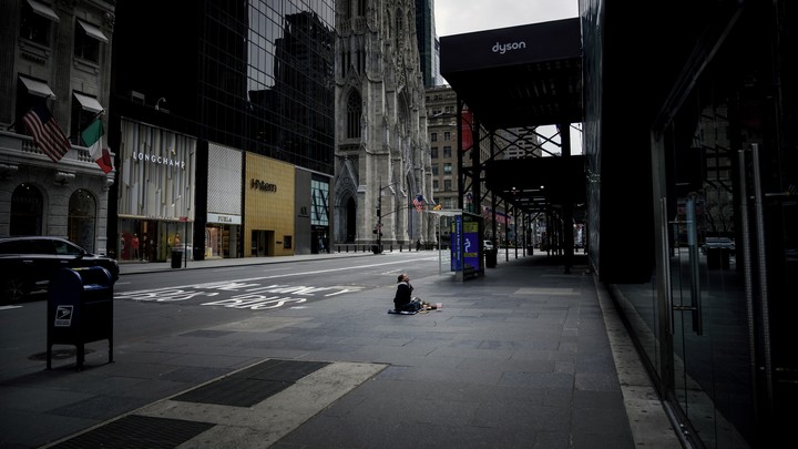 A homeless woman surrounded by luxury stores on 5th Street in New York City.