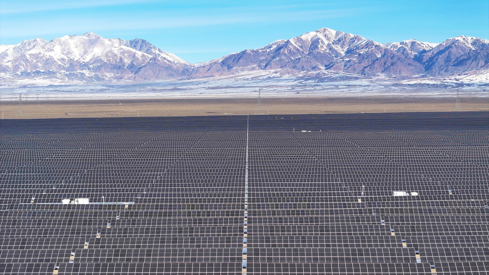 Vast grids of solar panels, backdropped by snow-covered mountains.