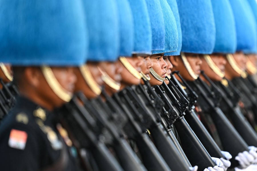 A long line of soldiers stand at attention while wearing dress uniforms that include tall, furry blue hats.