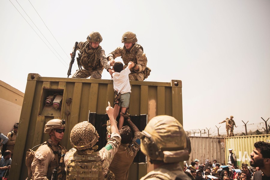 Soldiers lift a child up onto a container surrounded by people hoping to be evacuated from Kabul.