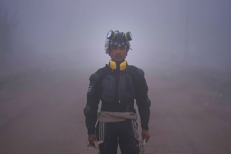 A person stands on a road, wearing protective gear and a gas mask on their head.
