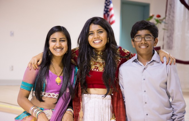 Two teenage girls and one teenage boy, dressed up, smile with their arms around each other
