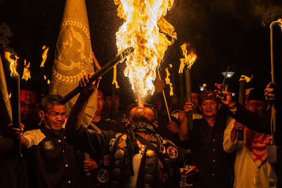 A person spits out flammable liquid, which burns in a fireball, as others hold torches nearby.