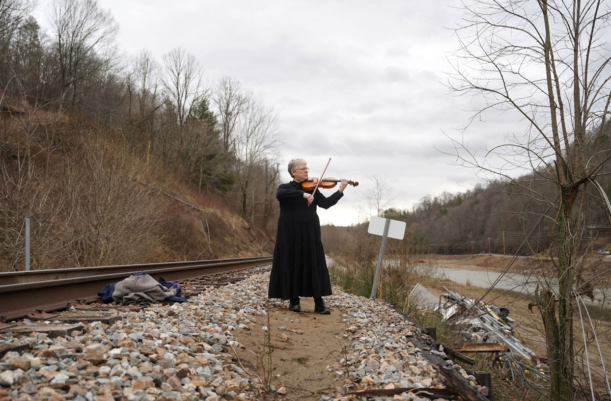 A person stands beside railroad tracks, playing a fiddle.