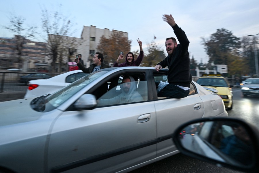 People cheer while riding in a car, several sitting in the open windows.