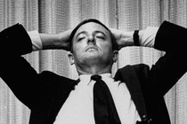 William F. Buckley sits with his hands placed behind his head.