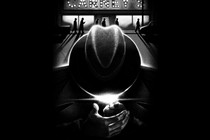 Black-and-white illustration of man lighting cigarette with hat down in foreground, with "Carney's" storefront in lights and long-shadowed silhouettes of men walking in distance behind
