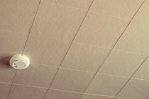 A beige tiled ceiling with a smoke alarm on it