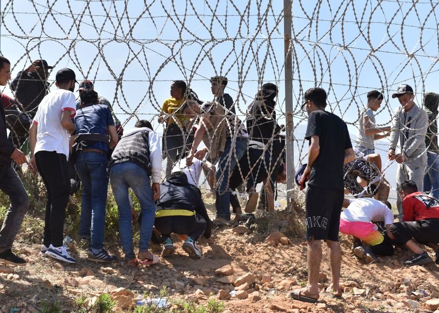 Migrants crawl under a fence.