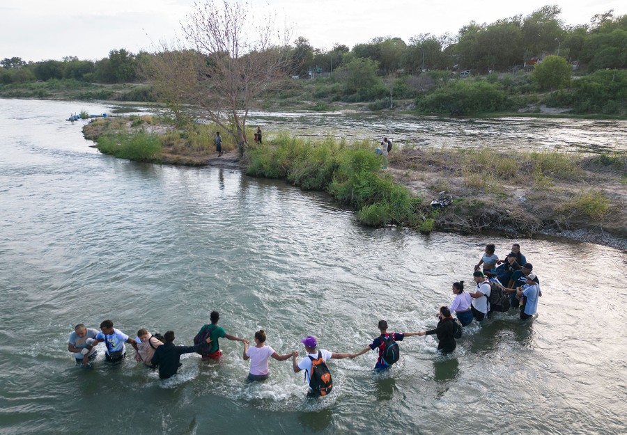 About a dozen people hold hands while crossing a waist-deep section of a river.