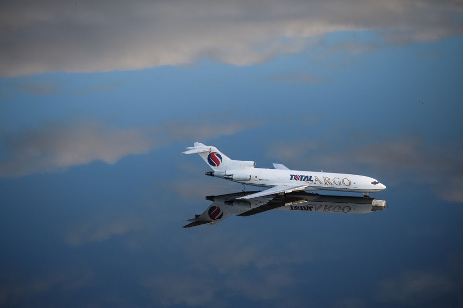 A passenger aircraft sits on flooded tarmac. The floodwater is very calm and reflects the sky and clouds above.