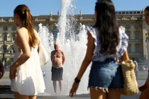 Women look on as a man stands in a fountain to cool off on a hot summer day.