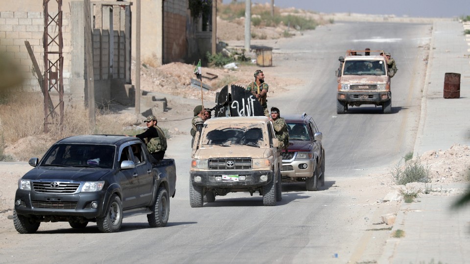 Turkey-backed Syrian rebel fighters ride on vehicles on a dusty road.