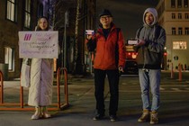 Three people hold up signs on placards and their mobile phones