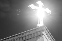 A cross on a rooftop, the sun illuminating it from behind