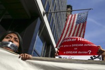 A young woman with tape on her mouth that reads "Hungry4aDream" stands in front of an American flag. 