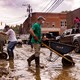 People clean up a muddy downtown street using wheelbarrows