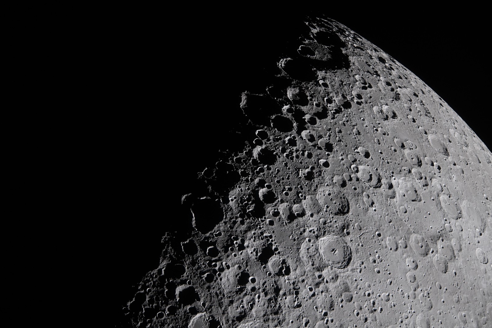 A close view of the surface of the moon, with many visible rugged craters along the line between shadow and sunlight