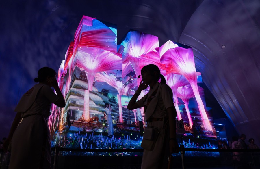 People walk past a large structure that has colorful images projected on its sides.