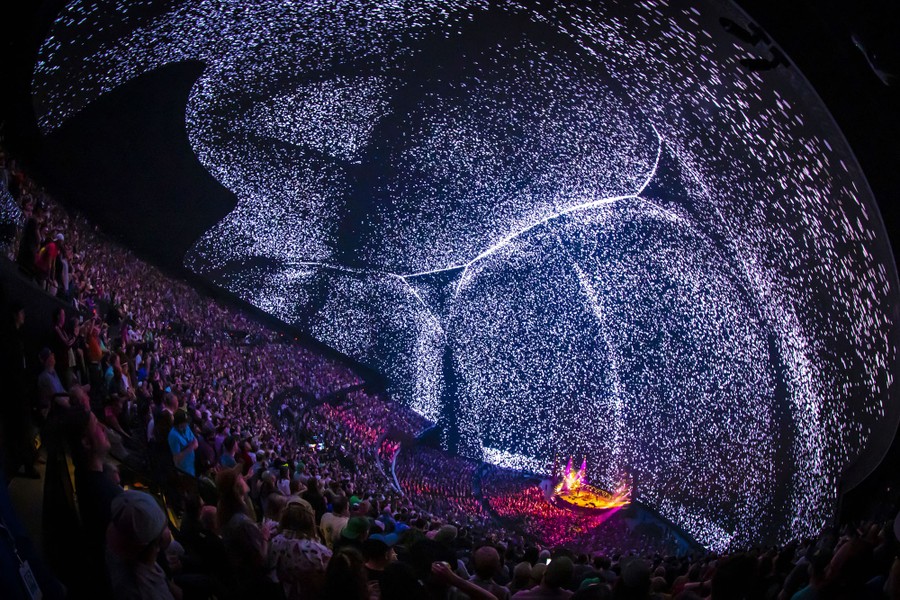 A view of the interior of a large sphere-shaped concert hall with a full audience and light projections on the walls