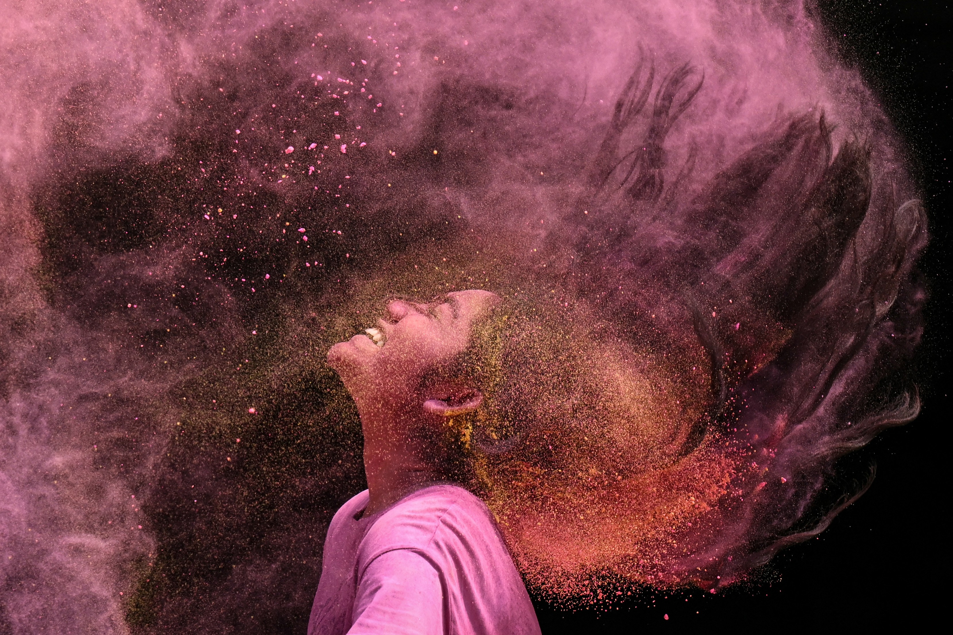 A girl smeared with colored powder flips her hair back, sending up a cloud of powder.