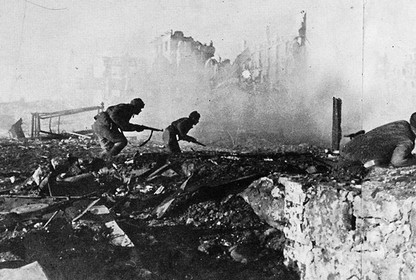 Armed soldiers advance amongst the rubble and smoke of a devastated city
