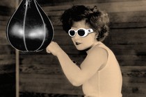 A woman in "clout goggles" (white sunglasses) hits a punching bag.