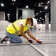 A construction worker kneels on the floor of a large room.