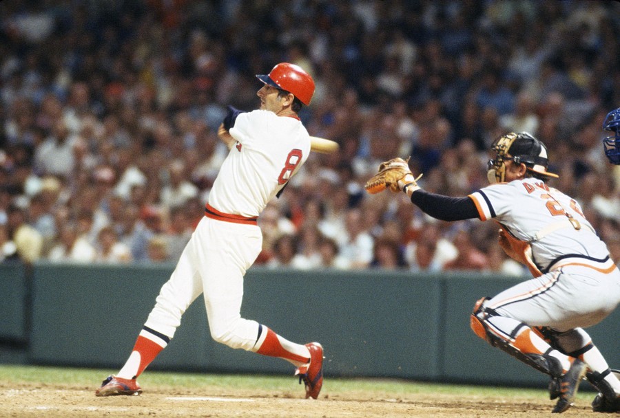 A baseball player swings his bat, having just hit a pitch.