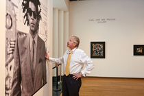 A man looking at a large portrait of Basquiat in museum gallery with two paintings hanging in the background.