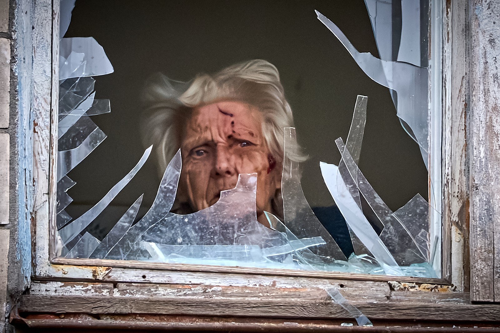 An injured woman looks out of her broken window after an apartment building was hit by a Russian drone.