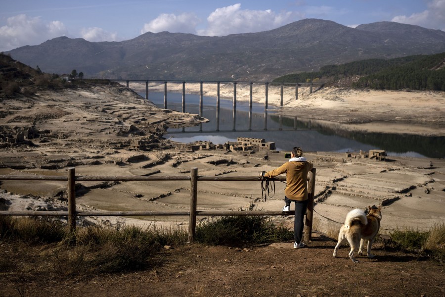 A person stands at a lookout point above a ruined village along a body of water that had recently reemerged after water levels dropped severely.