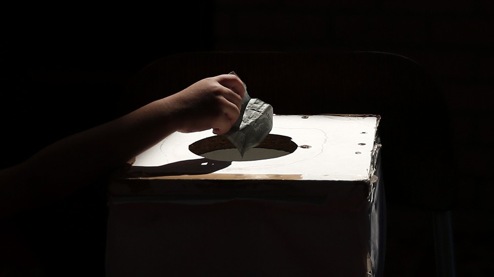 A hand drops money into a box.