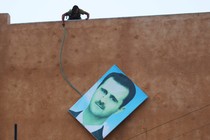 A rebel fighter stands atop a building and takes down a large picture of Assad after rebels captured the area in 2015.