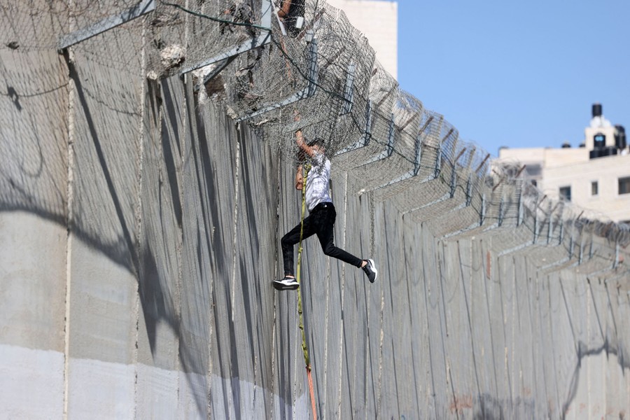 A person climbs down from a tall concrete border wall, using a rope.