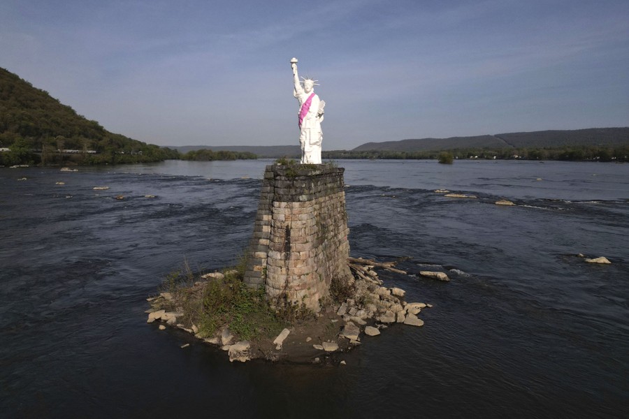 A miniature replica of the Statue of Liberty stands atop an old bridge support in a river.