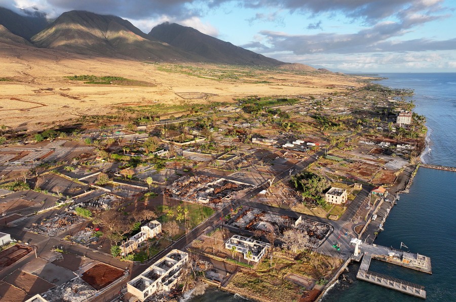 An aerial view of a small Hawaiian town, made up mostly of destroyed buildings and empty plots, one year after a wildfire