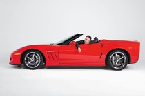 A man site in a red convertible with a sad expression on his face.