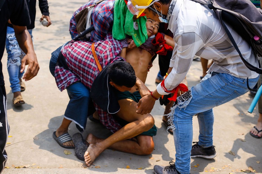 Several people carry a wounded man in a city street.