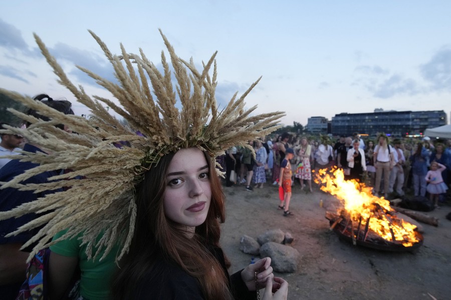 A woman wearing a wreath made of many tall stalks gathers with others around a bonfire.